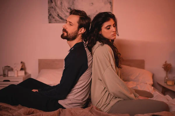 Triste casal com crise de relacionamento sentado na cama em casa à noite — Fotografia de Stock