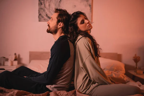 Homem descontente sentado de costas para trás com a namorada na cama à noite — Fotografia de Stock
