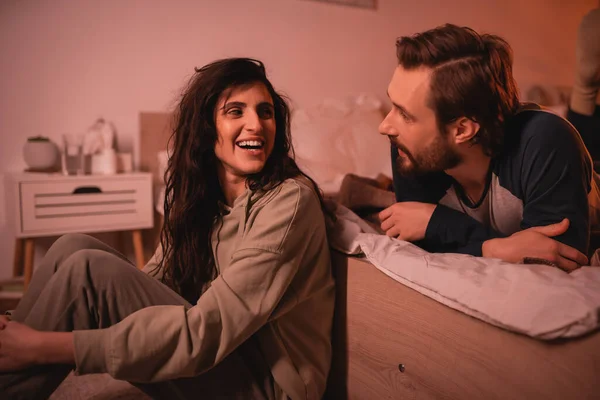 Bärtiger Mann spricht abends mit fröhlicher Freundin im Schlafzimmer — Stockfoto