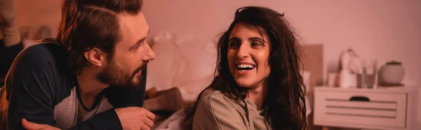 Mujer morena alegre hablando con novio barbudo en el dormitorio por la noche, pancarta - foto de stock