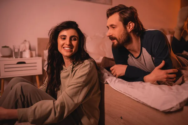 Bearded man talking to carefree girlfriend in bedroom in evening — Stock Photo