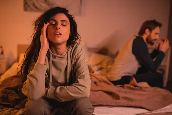 Tired woman sitting near blurred boyfriend on bed in evening — Stock Photo