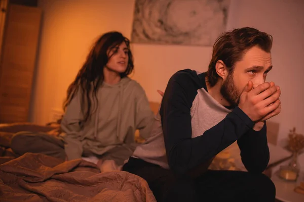 Tensed man sitting near blurred girlfriend in bedroom in evening — Stock Photo
