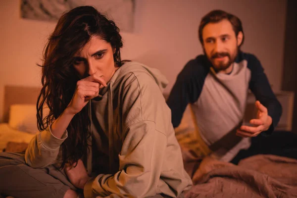 Frustrated woman sitting near boyfriend quarreling in bedroom in evening — Stock Photo