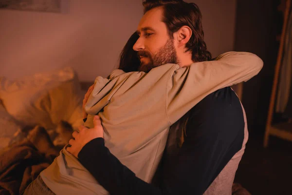 Bearded man hugging and calming down girlfriend in bedroom at night — Stock Photo
