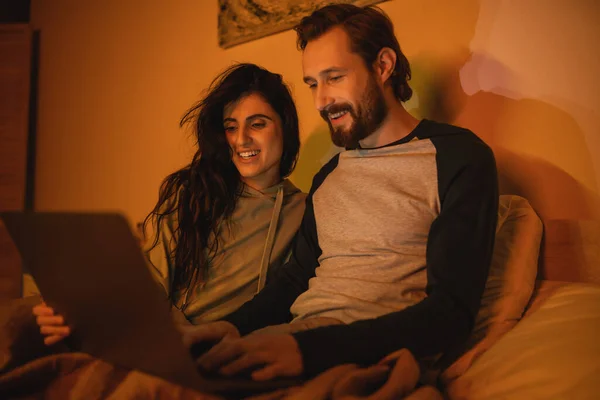 Безтурботна пара використовує розмитий ноутбук на ліжку вночі — стокове фото