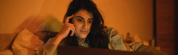 Femme brune regardant un film sur un ordinateur portable flou dans la chambre à coucher la nuit, bannière — Photo de stock
