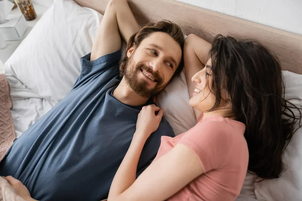 Top view of smiling brunette woman looking at bearded boyfriend on bed in morning — Stock Photo