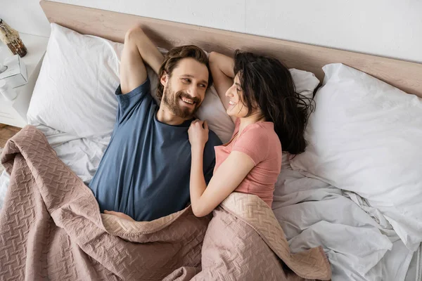 Вид зверху на насолодженого чоловіка, який дивиться на дівчину брюнетки, лежачи на ліжку вдома — стокове фото