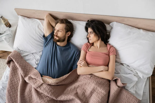 Draufsicht der unzufriedenen Frau, die die Arme verschränkt und ihren Freund zu Hause im Bett ansieht — Stockfoto