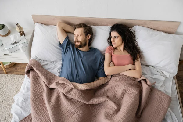 Visão superior da mulher morena insatisfeita olhando para namorado barbudo na cama em casa — Fotografia de Stock