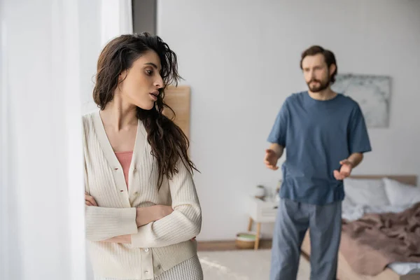 Displeased woman crossing arms near blurred boyfriend quarrelling at home — Stock Photo
