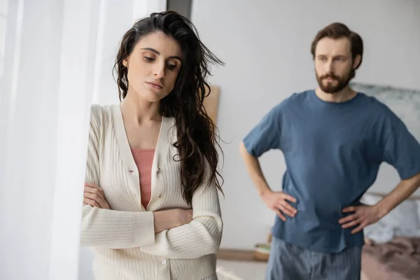 Грустная женщина, стоящая рядом с размытым парнем во время отношений трудности дома — стоковое фото