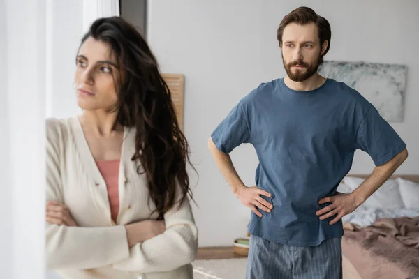 Bärtiger Mann im Pyjama blickt unzufriedene Freundin an, die zu Hause die Arme verschränkt — Stockfoto