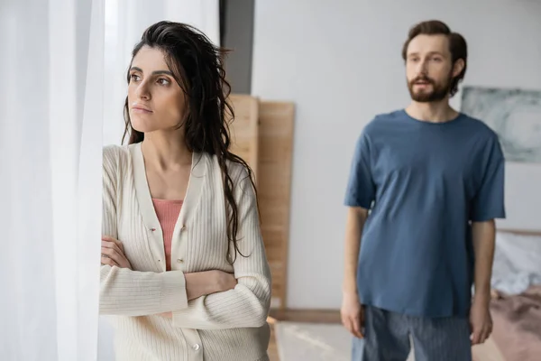 Offended woman standing near curtain while blurred boyfriend talking at home — Stock Photo