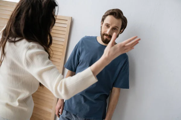 Frustrierter Mann im Pyjama steht neben verschwommener Freundin und streitet zu Hause — Stockfoto