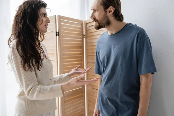 Vista lateral de la mujer morena hablando con su novio enojado en casa - foto de stock