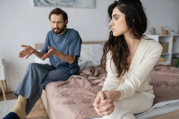 Sad woman sitting near blurred angry boyfriend talking in bedroom — Stock Photo