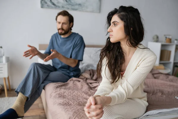 Offended woman sitting near blurred boyfriend talking during relationship difficulties at home — Stock Photo