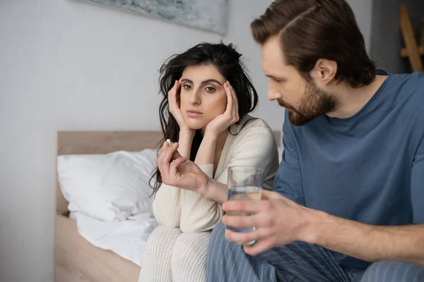 Pflegender Mann hält Tabletten und Wasser in der Nähe frustrierter Freundin zu Hause im Bett — Stockfoto