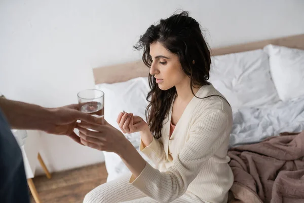 Homme attentionné donnant de l'eau à sa petite amie avec pilule assise sur le lit le matin — Photo de stock