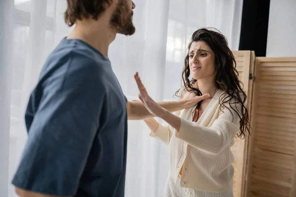 Scared woman showing stop gesture near abusive boyfriend at home — Stock Photo