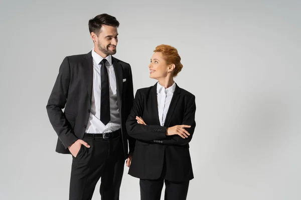 Задоволені ділові партнери в чорному формальному одязі посміхаються один одному ізольовані на сірому — стокове фото