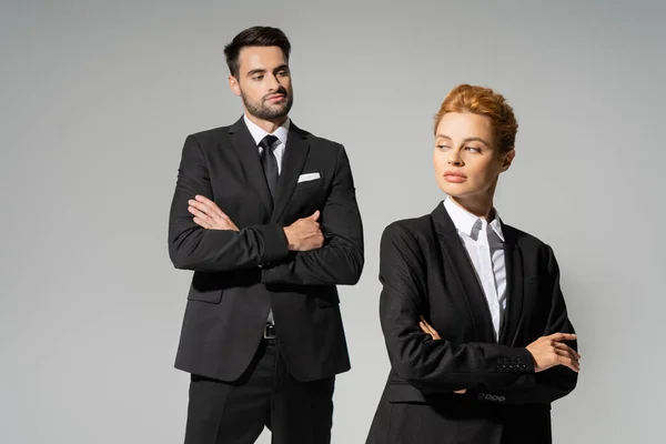Скептичний бізнесмен у стильному костюмі, дивлячись на руду жінку в офіційному одязі ізольовано на сірому — стокове фото