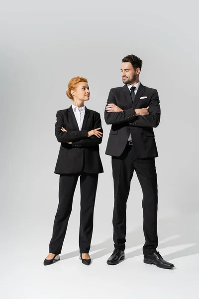 Full length on successful business partners in black pantsuits smiling at each other on grey background — Stock Photo