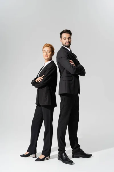 Full length of incredulous business people standing back to back with folded arms on grey background — Stock Photo