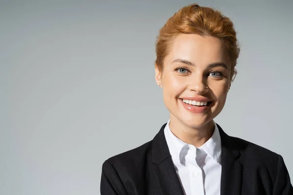 Portrait of overjoyed businesswoman with red hair smiling at camera isolated on grey — Stock Photo
