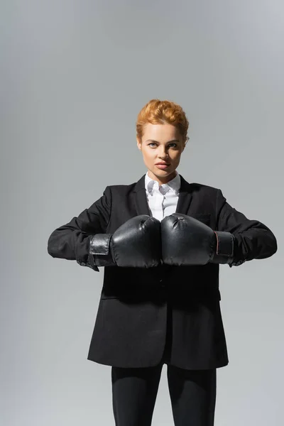 Entschlossene Geschäftsfrau in Boxhandschuhen und schwarzem Festkleid vereinzelt auf grau — Stockfoto