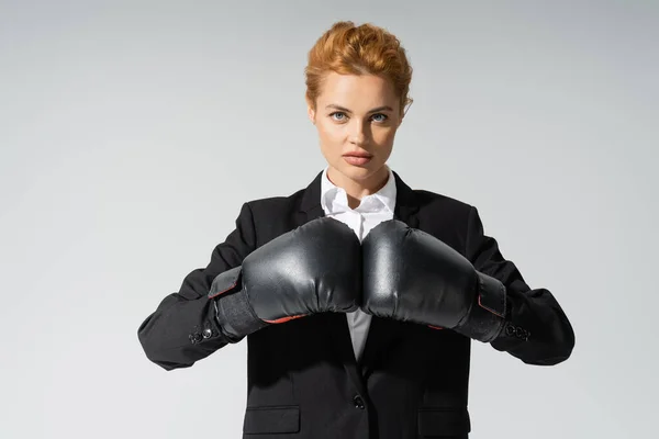 Seria donna d'affari in abbigliamento formale e guanti da boxe guardando la fotocamera isolata su grigio — Foto stock