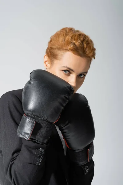 Rossa donna d'affari oscura il viso con i guanti da boxe mentre guarda la fotocamera isolata su grigio — Foto stock