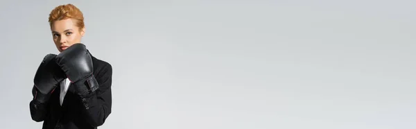 Sério ruiva empresária posando em luvas de boxe enquanto olha para a câmera isolada em cinza, banner — Fotografia de Stock