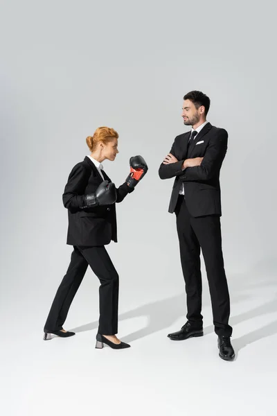 Confident businessman standing with folded arms near business competitor in boxing gloves on grey background — Stock Photo