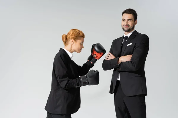Ruiva mulher em uso formal de boxe perto de empresário alegre de pé com braços cruzados isolados em cinza — Fotografia de Stock