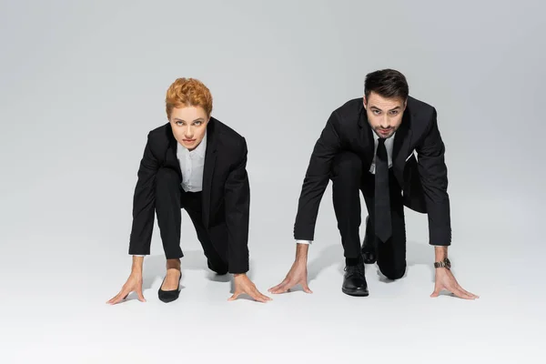 Стильные деловые люди в черных брюках, стоящие в низком стартовом положении и смотрящие в камеру на сером фоне — стоковое фото