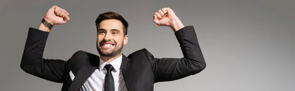 Успішний і задоволений бізнесмен, що показує жест тріумфа ізольований на сірому, банер — стокове фото