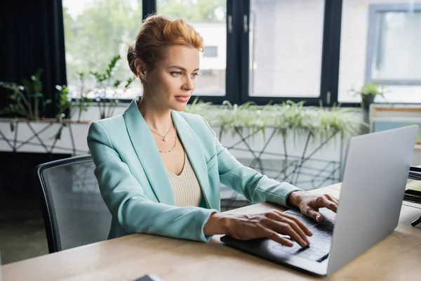Empresária em blazer elegante digitação no laptop no escritório moderno — Fotografia de Stock