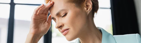 Mujer de negocios cansada con los ojos cerrados sosteniendo la mano cerca de la frente y sufriendo de dolor de cabeza en la oficina, pancarta - foto de stock