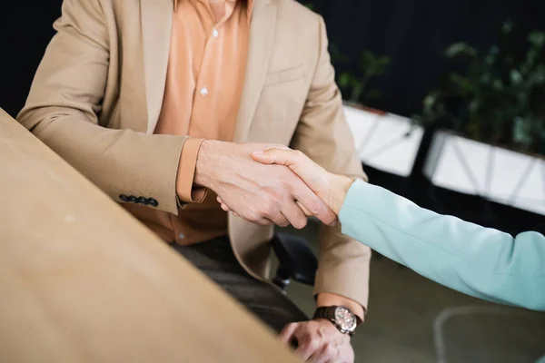 Частичный взгляд деловых партнеров, пожимающих руки на размытом переднем плане в офисе — стоковое фото