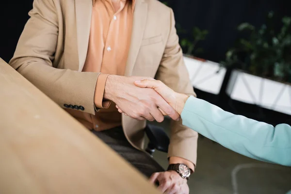 Partial view of business partners shaking hands on blurred foreground in office — Stock Photo