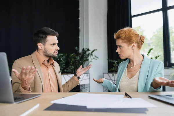 Verwirrte Manager zeigen achselzuckende Geste, während sie in der Nähe von Dokumenten im Büro reden — Stockfoto