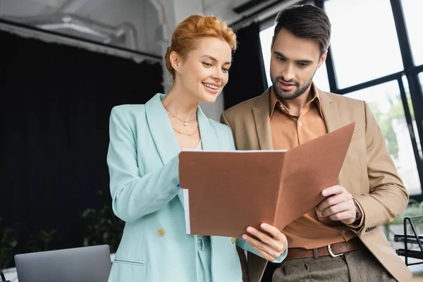 Happy business colleagues in stylish blazers looking at folder with documents in office — Stock Photo