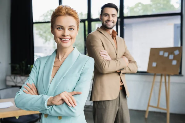 Joyful business partners in trendy blazers crossing arms and smiling at camera in office — Stock Photo