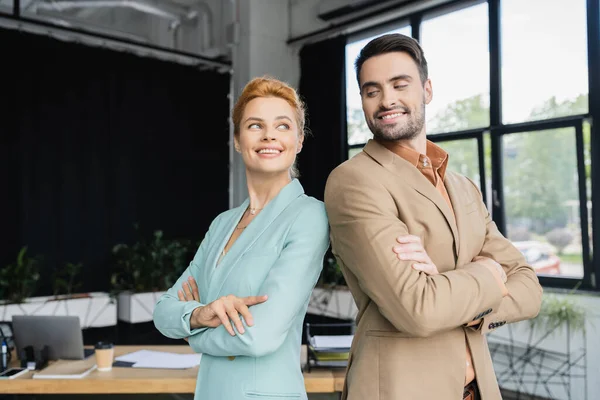 Веселые и стильные деловые коллеги, стоящие со сложенными руками и улыбающиеся в офисе — стоковое фото