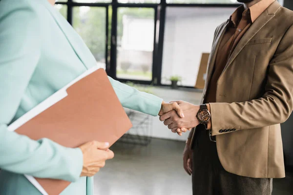 Cropped view of businesswoman with folder shaking hands with partner in office — Stock Photo