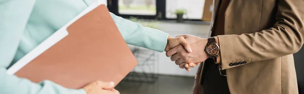 Partial view of woman with folder shaking hands with businessman in office, banner — Stock Photo