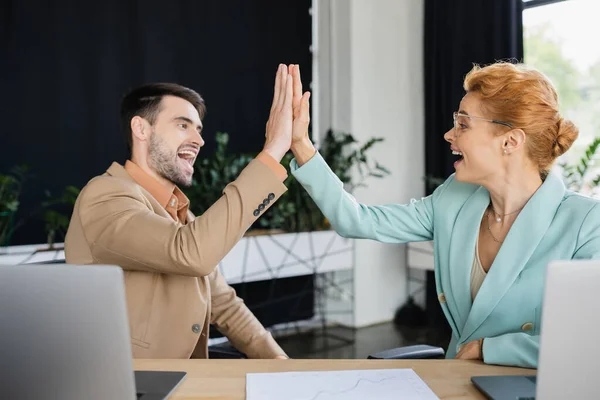 Excited and stylish business partners giving high five at workplace in office — Stock Photo